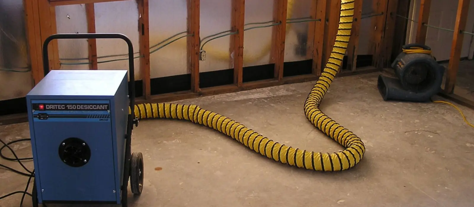 Dehumidifier and a yellow duct hose running beside opened walls